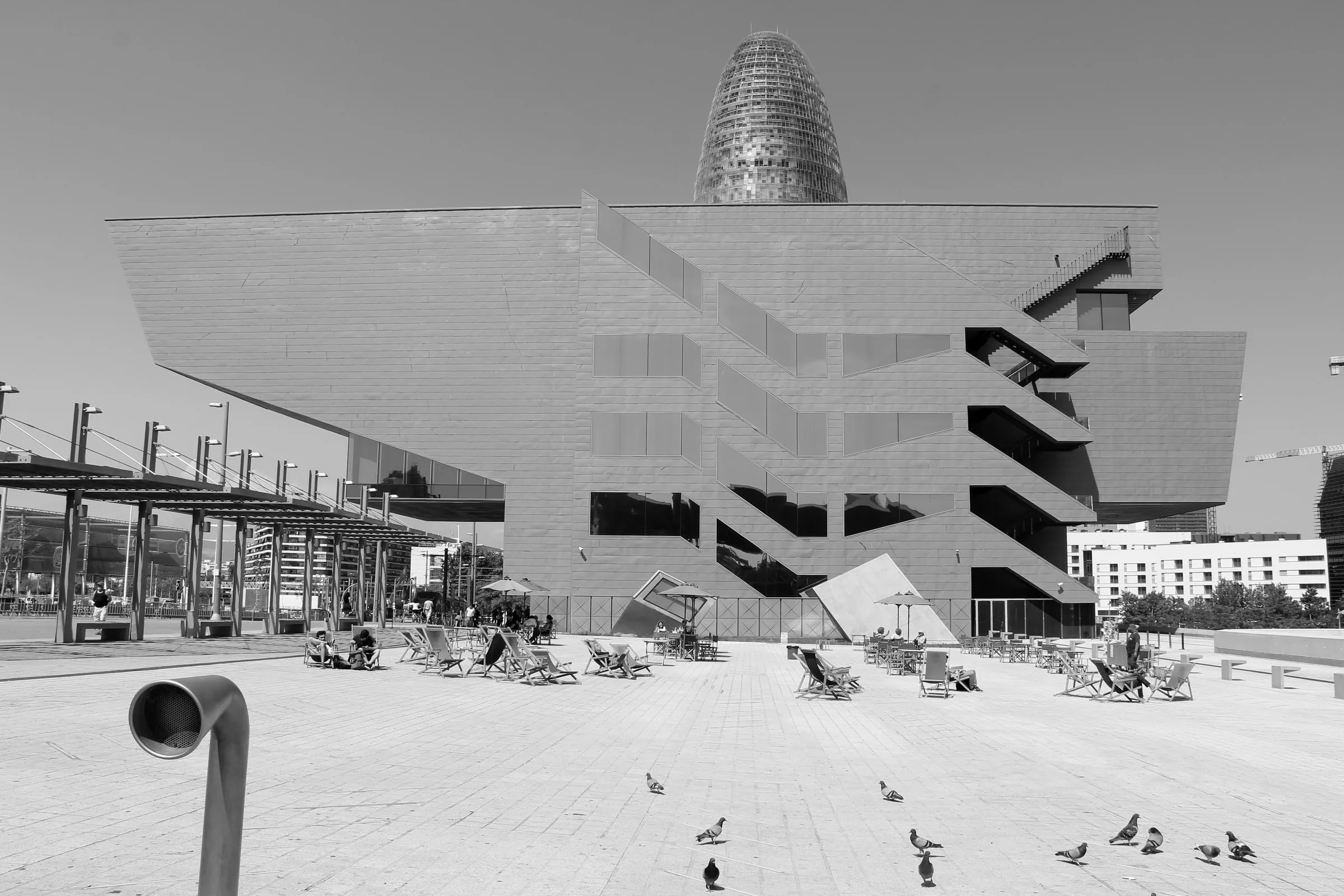 People in deckchairs on the plaza of the Disseny Hub in Poblenou, Barcelona, with Torre Glòries behind.